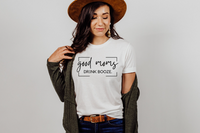 Good Moms tee in white paired with a white brimmed hat, green long sweater and medium wash jeans.